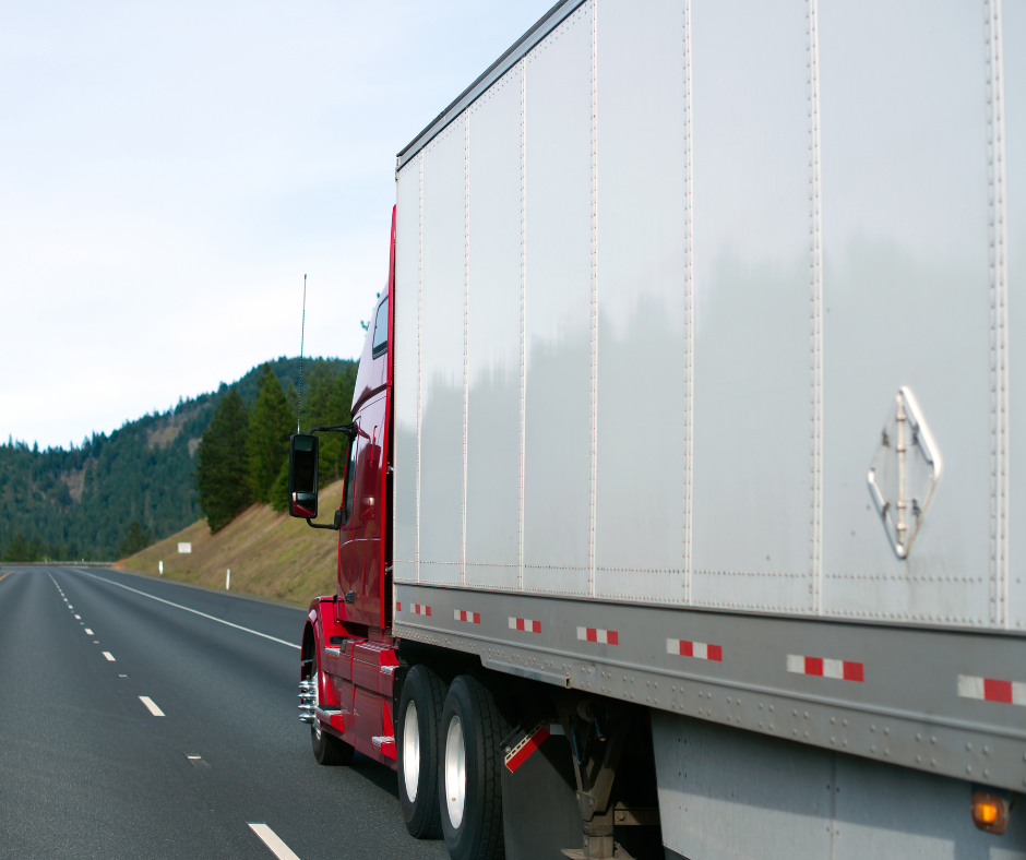 A red and white dry van truck drives through the frame on the open road in middle America.