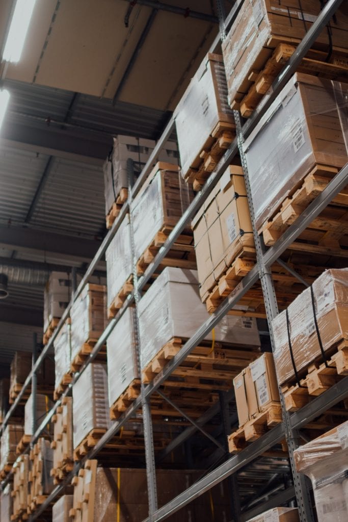 Multiple crates of product are stacked on shelves in a warehouse.